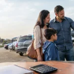 Cena ilustrativa de poupança e rendimentos: família brasileira olhando um carro usado em estacionamento aberto, com caderneta sem texto e calculadora sobre mesa em primeiro plano