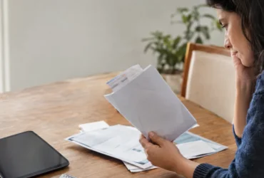 Cena ilustrativa de investimentos e liquidez: mão de consumidor com envelope de despesas médicas sem textos e tablet desligado ao lado de documentos financeiros genéricos