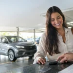 Cena ilustrativa de aluguel de veículos e cartão: carro alugado genérico em estacionamento iluminado, chave sobre balcão de locadora e cartão sem marca ao lado de contrato ilegível