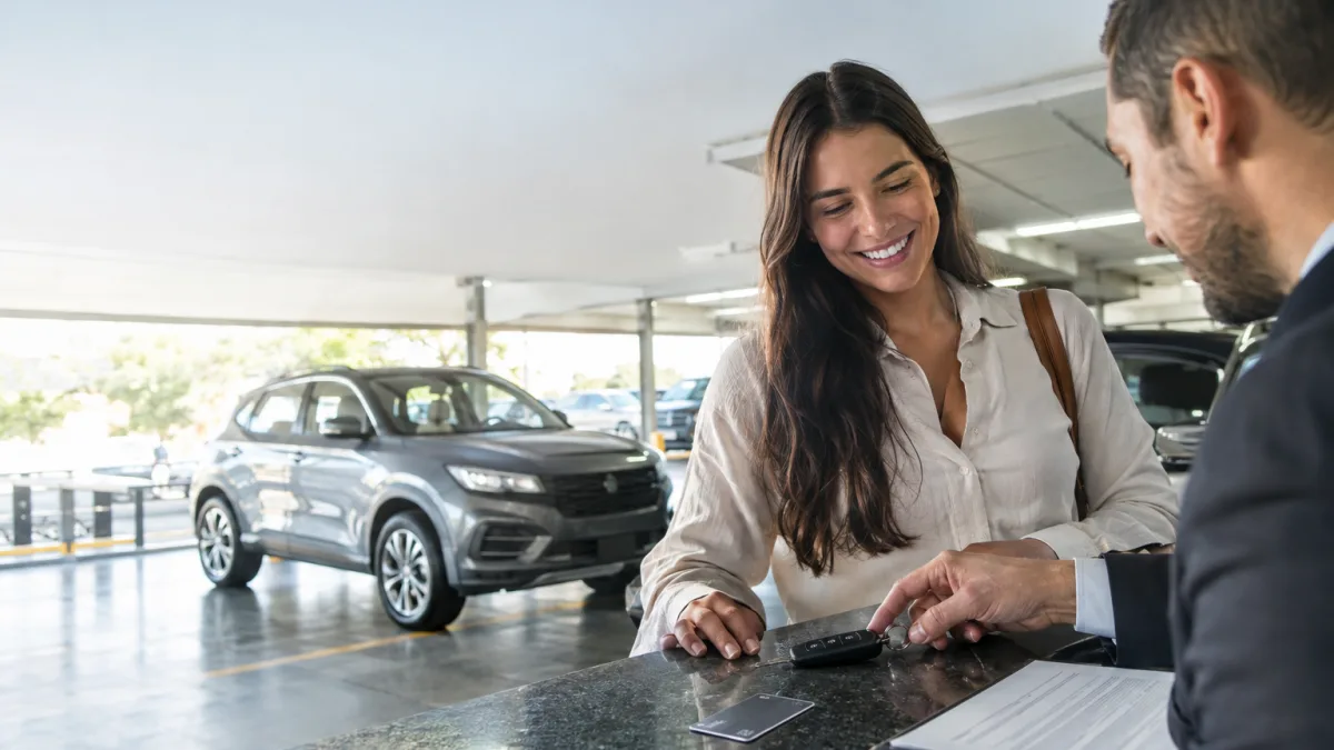 Cena ilustrativa de aluguel de veículos e cartão: carro alugado genérico em estacionamento iluminado, chave sobre balcão de locadora e cartão sem marca ao lado de contrato ilegível