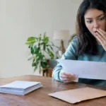 Cena ilustrativa de renegociação e quitação: mesa com envelope de acordo financeiro sem letras, pilha de comprovantes em branco e pessoa surpresa diante de correspondência genérica