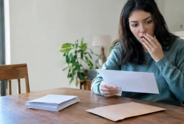 Cena ilustrativa de renegociação e quitação: mesa com envelope de acordo financeiro sem letras, pilha de comprovantes em branco e pessoa surpresa diante de correspondência genérica