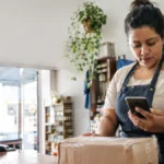 Cena ilustrativa de comércio e comprovante falso: balcão de pequena loja brasileira com pacote pronto para entrega, comerciante olhando extrato em smartphone com tela ilegível