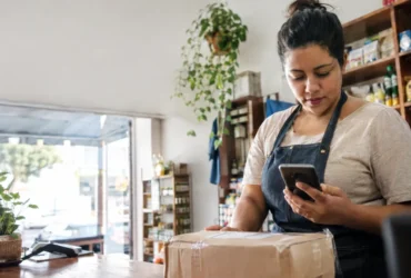 Cena ilustrativa de comércio e comprovante falso: balcão de pequena loja brasileira com pacote pronto para entrega, comerciante olhando extrato em smartphone com tela ilegível